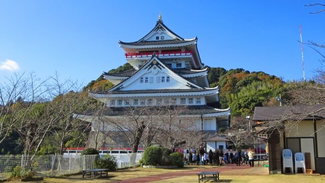 快晴の下にそびえる熱海城と芝生広場、観光客が並ぶ様子