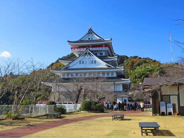快晴の下にそびえる熱海城と芝生広場、観光客が並ぶ様子
